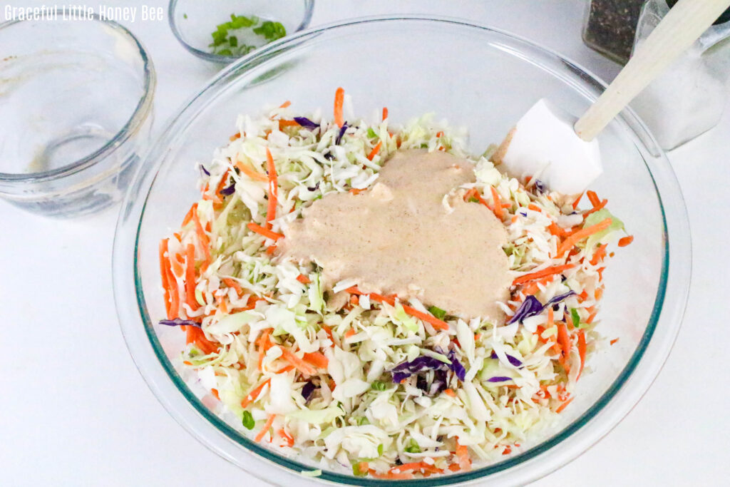 Shredded vegetables with dressing on top in clear mixing bowl.